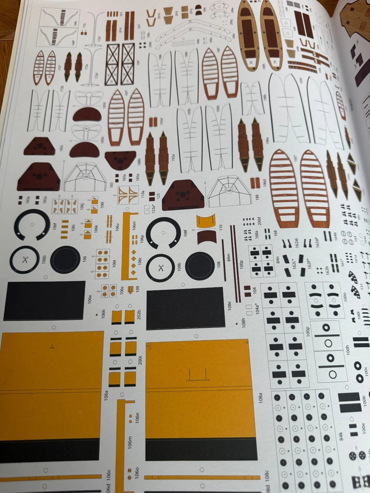 A printed decal sheet for a model boat, featuring various brown, black, and yellow cut-out pieces and markings on a white background.