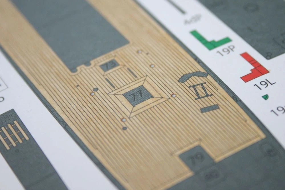 Close-up of a printed decal sheet with a tan wood-grain panel design, gray outlines, and small colored shape markers in green and red.