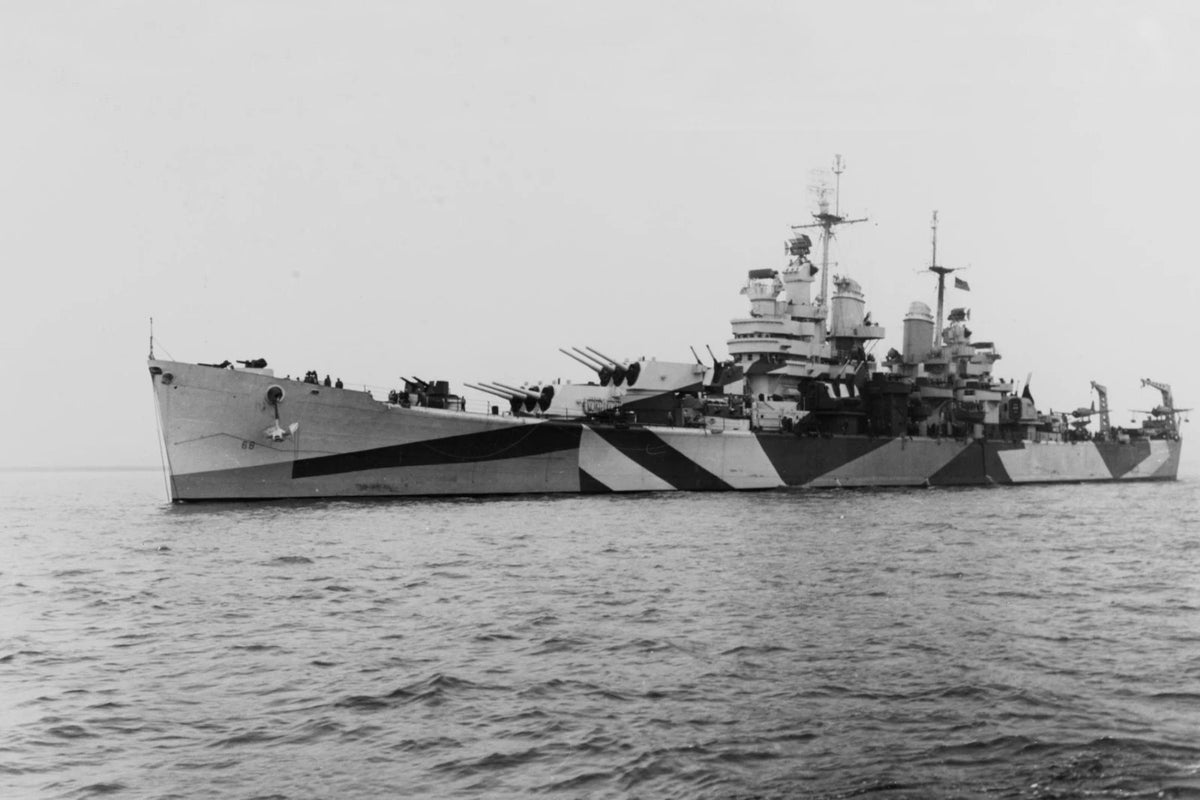 Black and white photograph of a military battleship at sea, showing the hull, superstructure, and surrounding ocean under a pale sky.