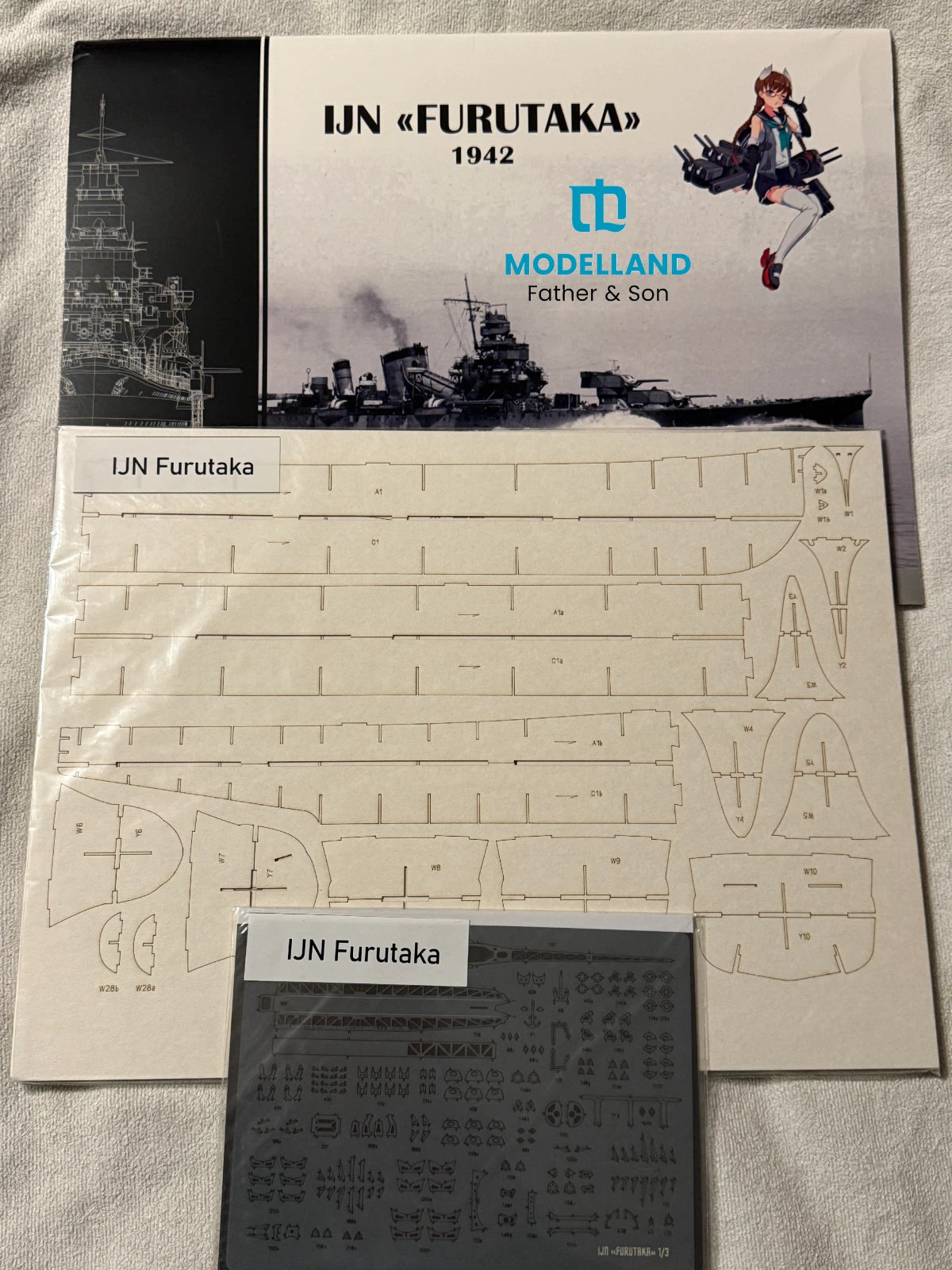 Model kit parts sheet and instruction booklet for an IJN Furutaka 1942 model ship, branded Modelland, displayed on a light fabric background.