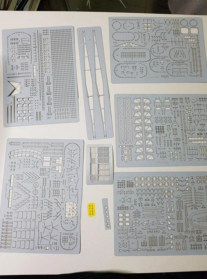 A set of light gray plastic model kit decal sheets and small parts laid out on a white surface, including various printed templates, strips, and tiny hardware pieces.