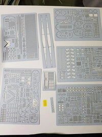 A set of light gray plastic model kit decal sheets and small parts laid out on a white surface, including various printed templates, strips, and tiny hardware pieces.
