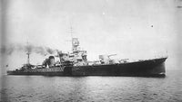 Black and white historical photograph of a large military battleship at sea, with smoke rising from its funnels and open ocean in the foreground.