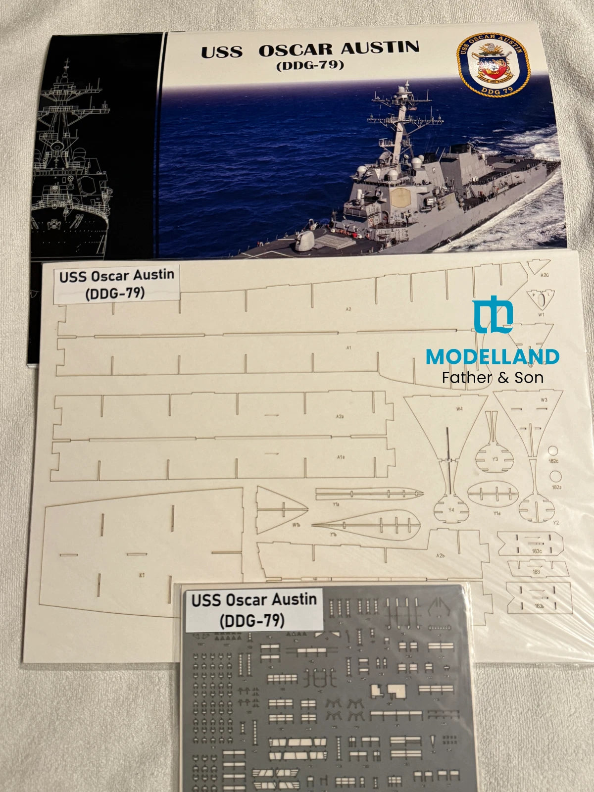 Model kit parts sheet for the USS Oscar Austin (DDG-79) from Modelland Father & Son, showing the printed layout sheet and a gray decal sheet on a white fabric background.