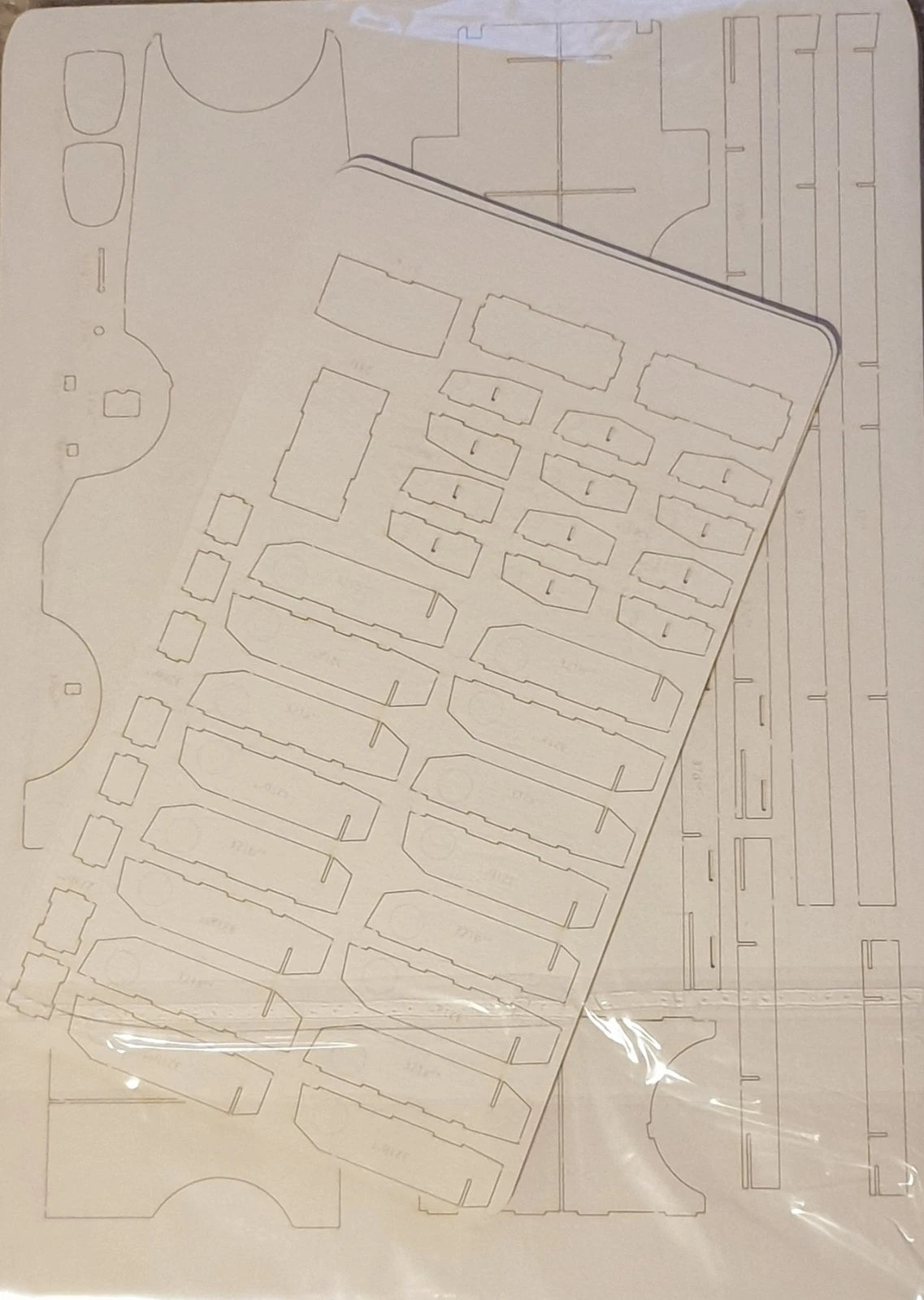 A laser-cut foam panel or craft sheet with multiple pre-cut slots and compartments, shown partially covered by a clear plastic protective sleeve.