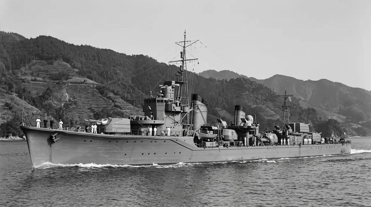 Black and white photograph of a military ship sailing on water with mountains in the background.