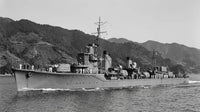 Black and white photograph of a military ship sailing on water with mountains in the background.