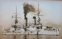 A vintage-toned photograph of a large naval battleship at sea, with smoke billowing from its funnels and a pale sky in the background.