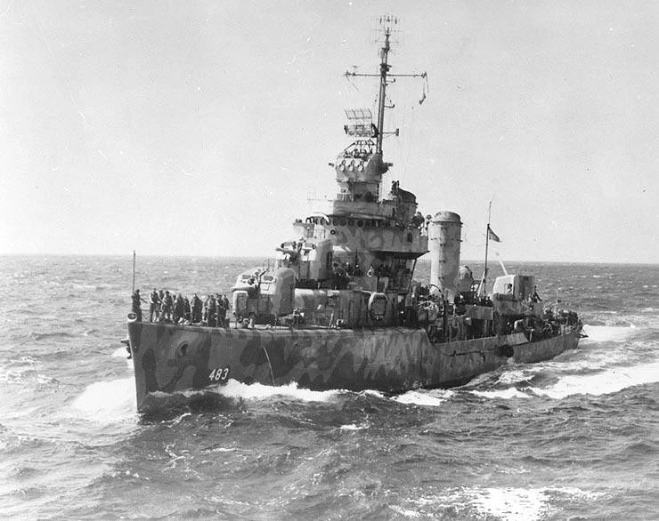Black and white historical photograph of a military warship sailing on open water, with crew visible on deck and a hazy sky above.