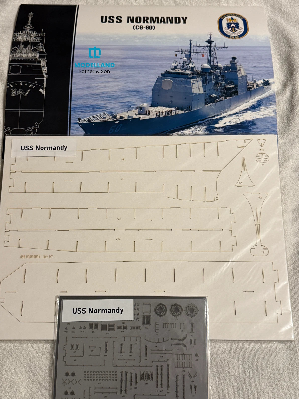 Model kit parts sheet and decal sheet for the USS Normandie (CG-68) model ship, displayed on a light gray fabric background.