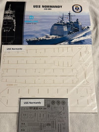 Model kit parts sheet and decal sheet for the USS Normandie (CG-68) model ship, displayed on a light gray fabric background.