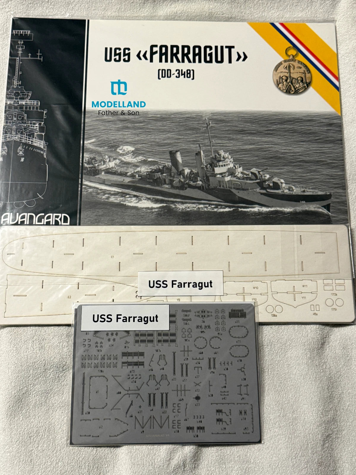 Alvargard Modelland USS Farragut (DD-348) model ship kit components laid out on a white fabric background, including the instruction booklet, white plastic parts sheet, and gray decals sheet labeled 'USS Farragut'.