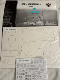 A model kit parts kit for the Russian battleship Tsar Peter I on a light fabric background. The kit includes a printed instruction sheet, a sheet of laser-cut plastic pieces, and a sheet of decals.